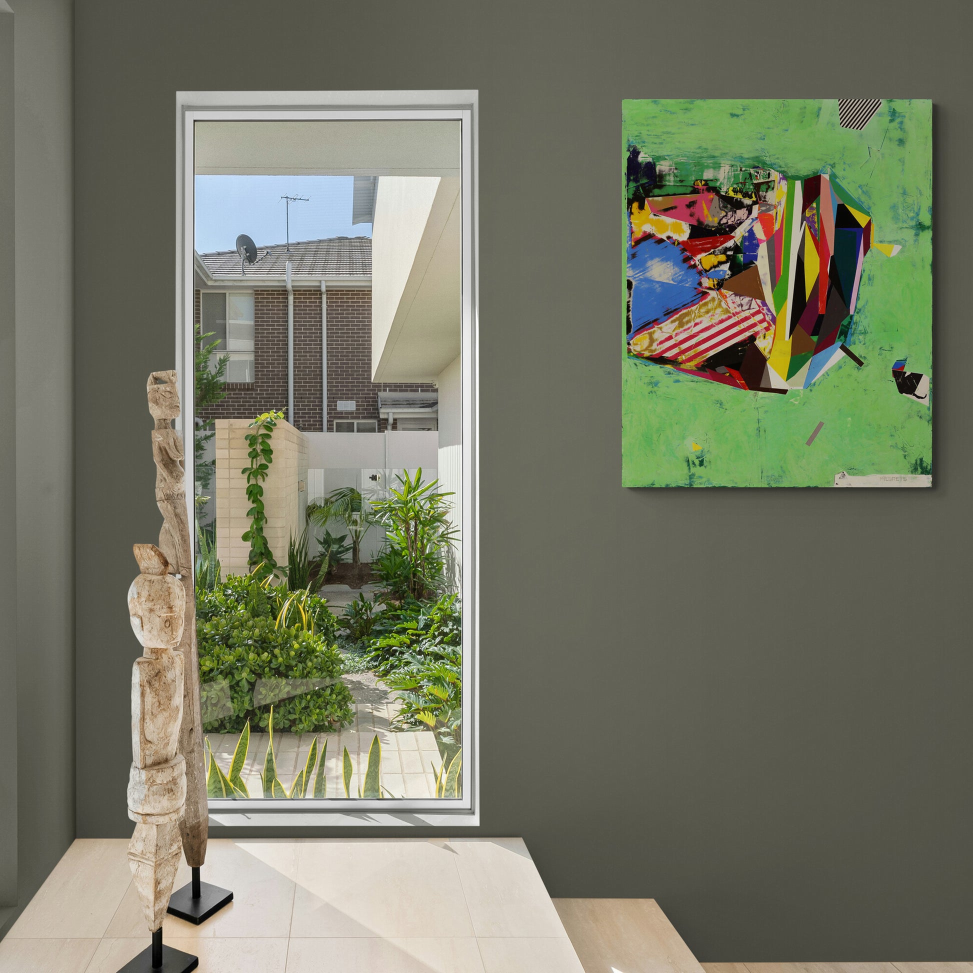 Modern interior with abstract painting, garden view, and totem-like sculpture.