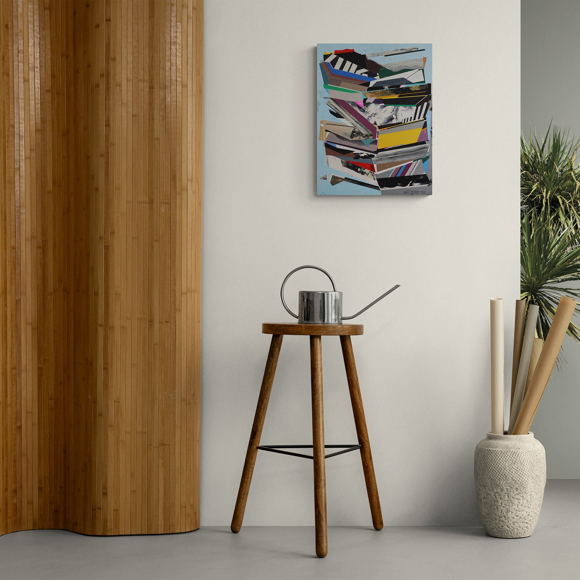 Contemporary art above a wooden stool with a watering can, against a light gray wall.