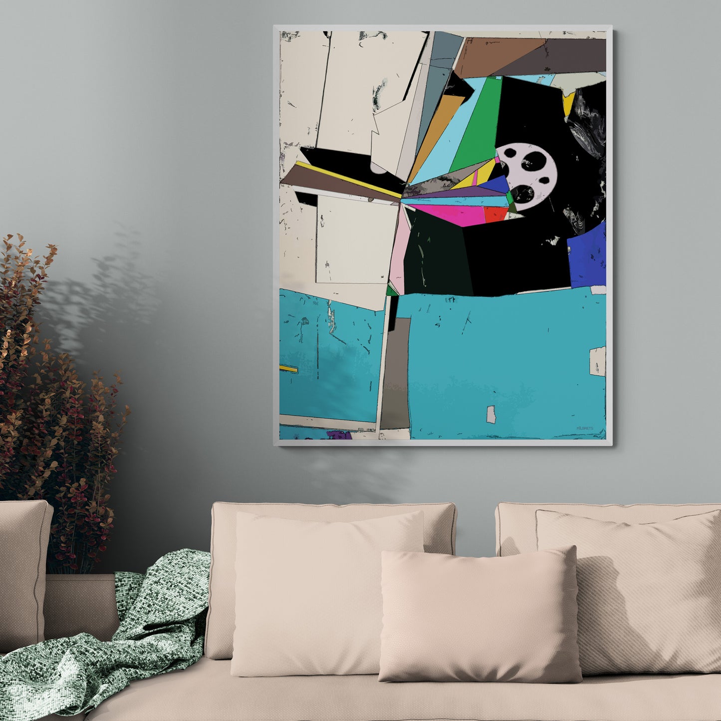 A framed abstract geometric wall art print with bold blocks of turquoise, black, cream, green, pink, and yellow, hanging on a gray wall above a beige sofa with pillows.