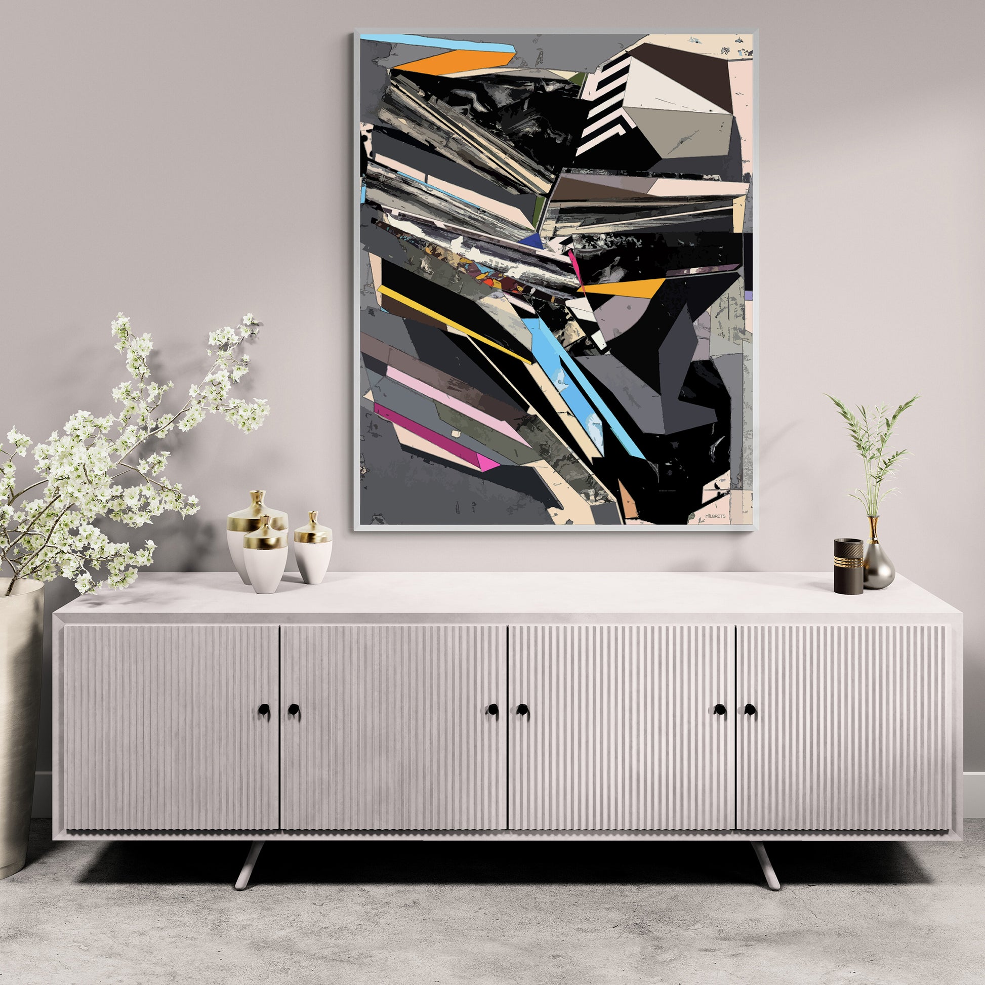 A framed abstract geometric wall art print with black, gray, white, blue, and pink shapes, displayed above a light gray ribbed sideboard cabinet in a styled room setting.