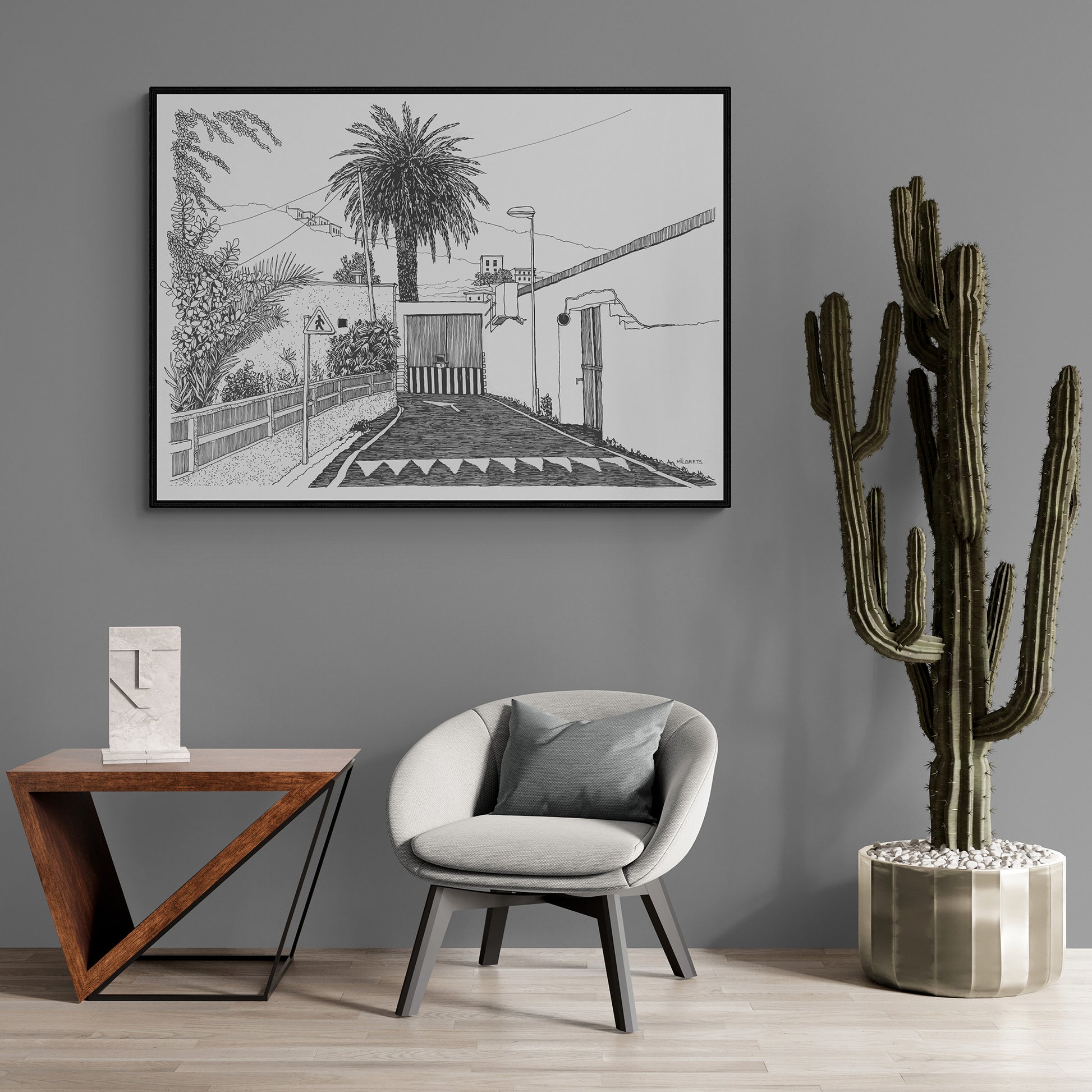 Modern living room with a gray armchair, wooden side table, and cactus plant against a gray wall with tropical framed artwork.