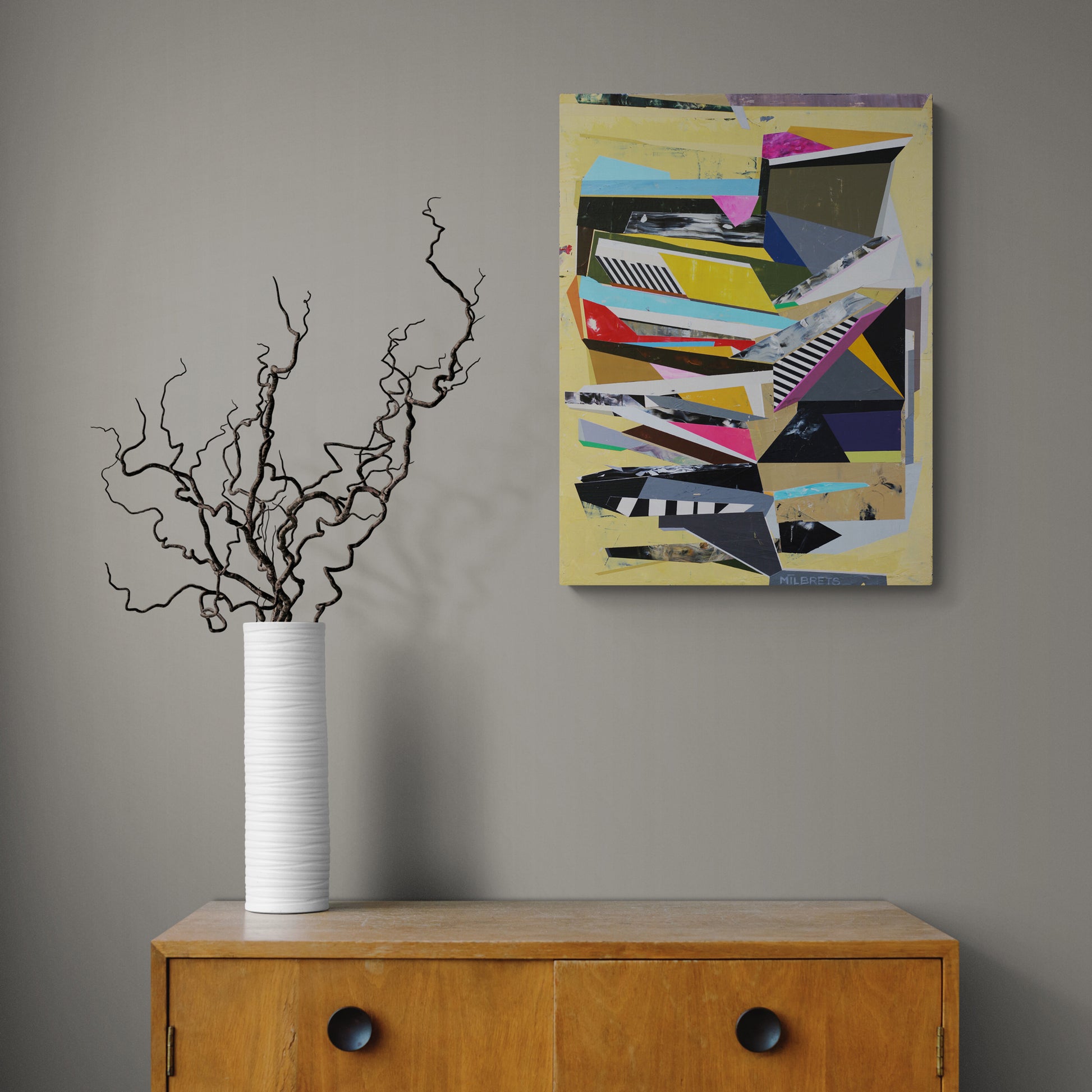 Abstract painting on a wall above a wooden cabinet with a vase and branches.